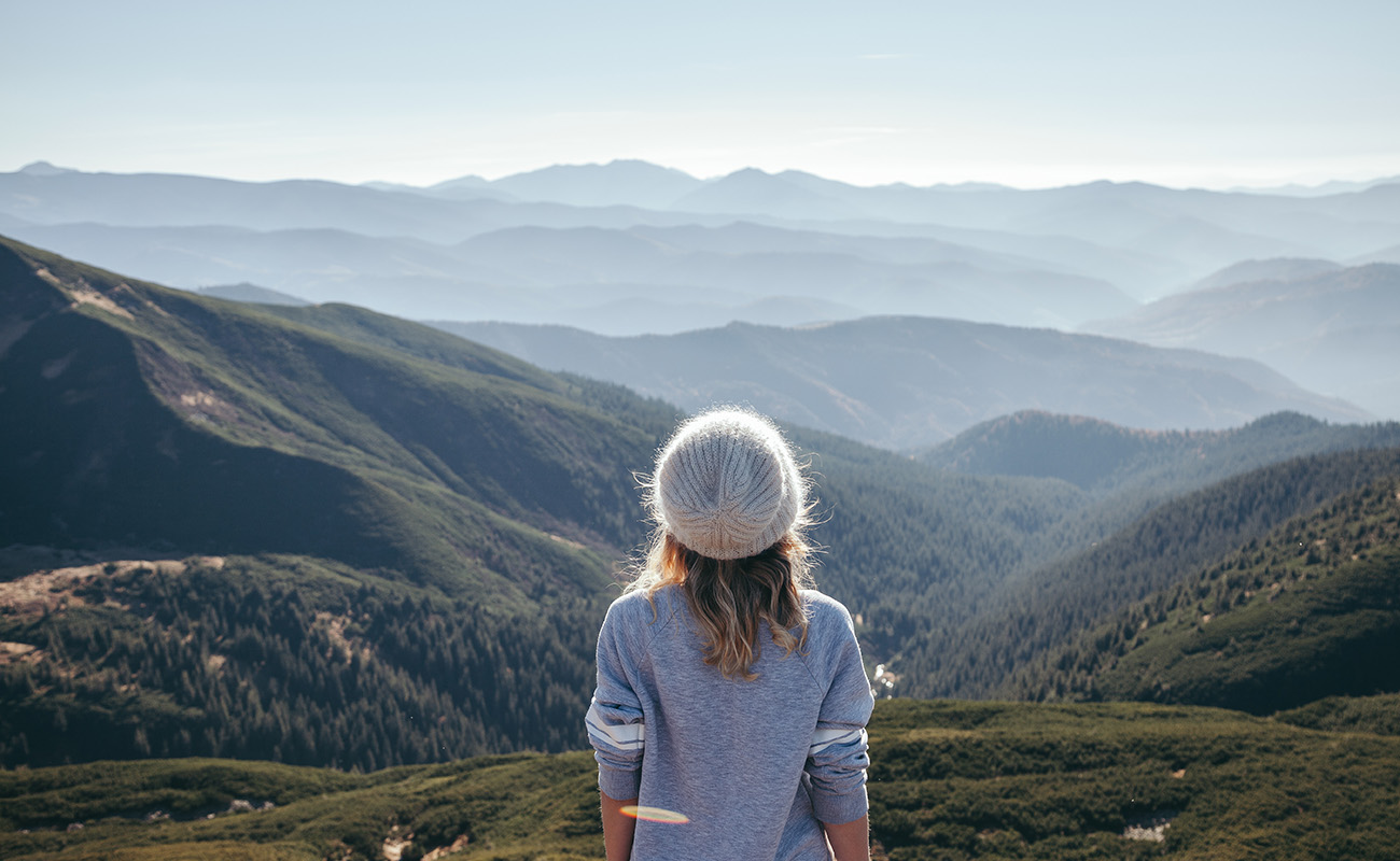 為了釋放工作壓力大，一名女性前往大自然，站在山巒間，享受寧靜的自然環境，遠眺連綿山景，尋求身心放鬆與平靜。